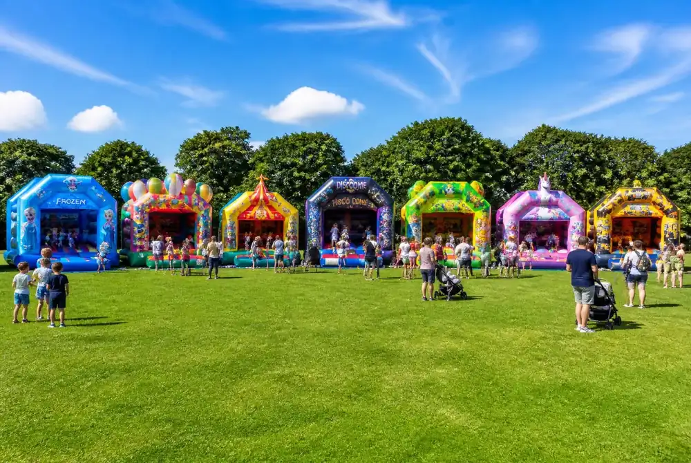 Sieben bunte Hüpfburgen von Sprung & Süß Verleih nebeneinander auf einer Wiese bei einem Familienevent